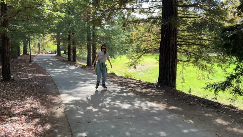 Beautiful young girl is rollerskating in a park wearing in blue jeans
