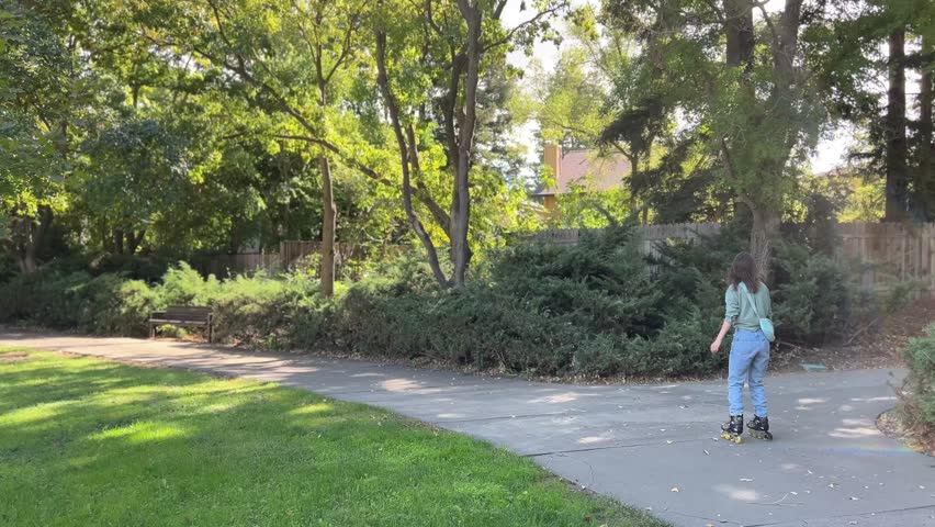 Beautiful young girl is rollerskating in a park wearing in blue jeans