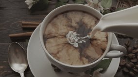 Pouring cream into black coffee in cup, with cinnamon sticks, coffee beans and flowers artfully arranged on rustic wooden table nearby. Close-up view - Powered by Shutterstock - Get 15% off with code: PIKWIZARD15