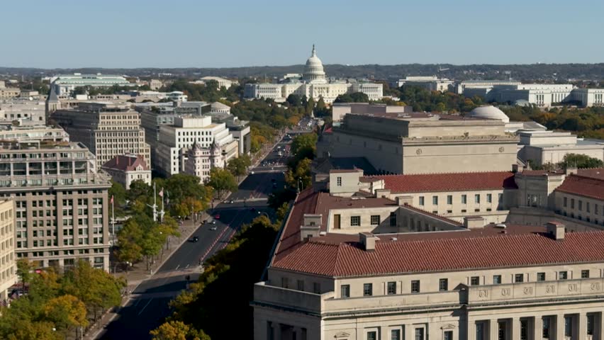 Aerial view of Washington DC with a street lined with trees and buildings, including the US Capitol in the distance.