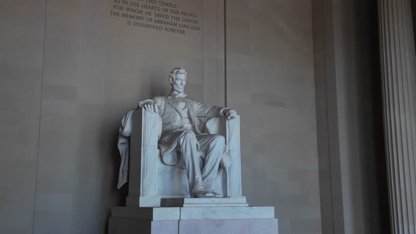 Closeup view of the Lincoln Memorial statue in Washington DC. The marble sculpture depicts Abraham Lincoln seated in a chair, with his hands resting on the armrests.