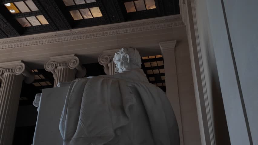 Closeup view of the Lincoln Memorial statue in Washington DC. The marble sculpture depicts Abraham Lincoln seated in a chair, with his hands resting on the armrests.