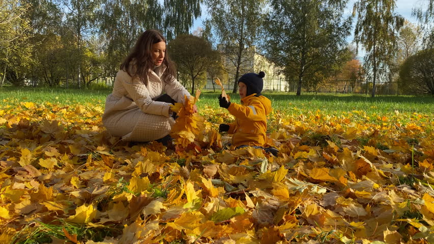 Mother and child outdoors have fun on the city park in autumn. Smiling woman with son on a sunny autumn day.