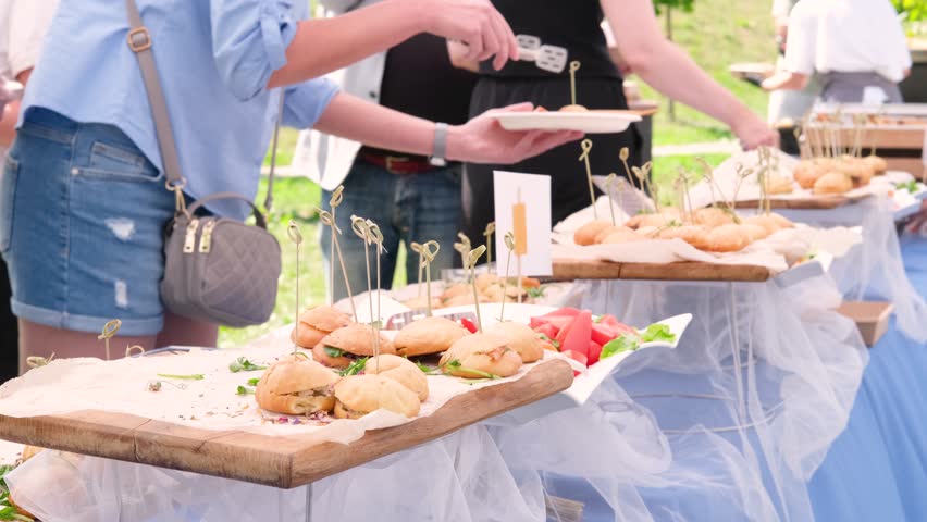 Guests help themselves to plates at an elegant open buffet. Attendees enjoy a variety of sandwiches under sunny skies. Perfect for events and lifestyle themes