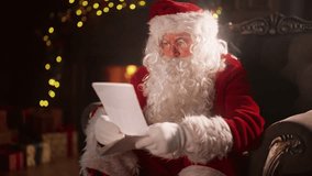 Magical Christmas, Santa Claus sitting at home and reading letters with wishes. Kind magician holding paper in hands when sitting in chair alone in Xmas night, warming near burning fireplace, portrait - Powered by Shutterstock - Get 15% off with code: PIKWIZARD15