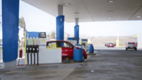 Blurred scene at a petrol station with a red car near fuel pumps under a canopy with other vehicles parked in the background - Powered by Shutterstock - Get 15% off with code: PIKWIZARD15