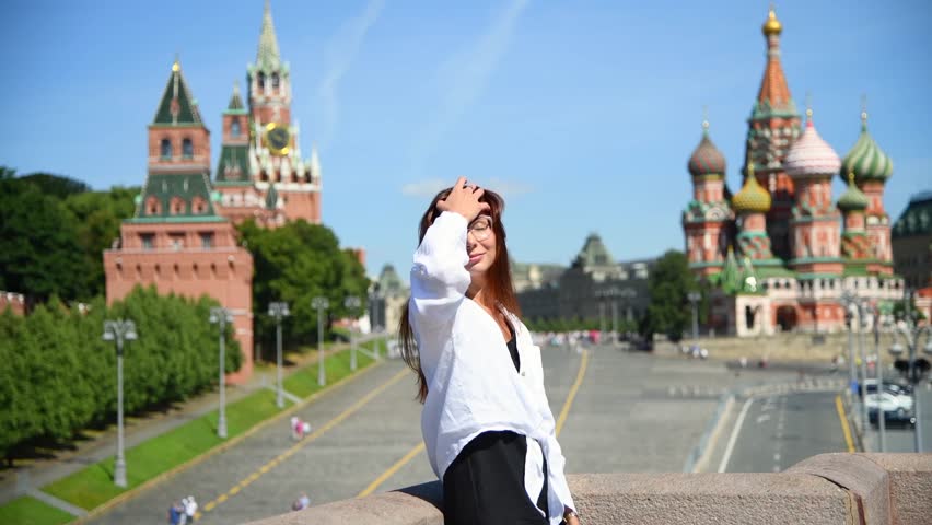 Side view portrait of happy beautiful brunette woman in eyeglasses, black dress and white shirt in a sunny summer day in Moscow, Russia. Moscow Kremlin and Saint Basil