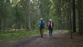 Senior couple enjoy Nordic walking with sticks on pathway in forest. Elderly positive man and woman stroll actively due to health caring. Energetic retirement marital pair smiling and admiring nature - Powered by Shutterstock - Get 15% off with code: PIKWIZARD15