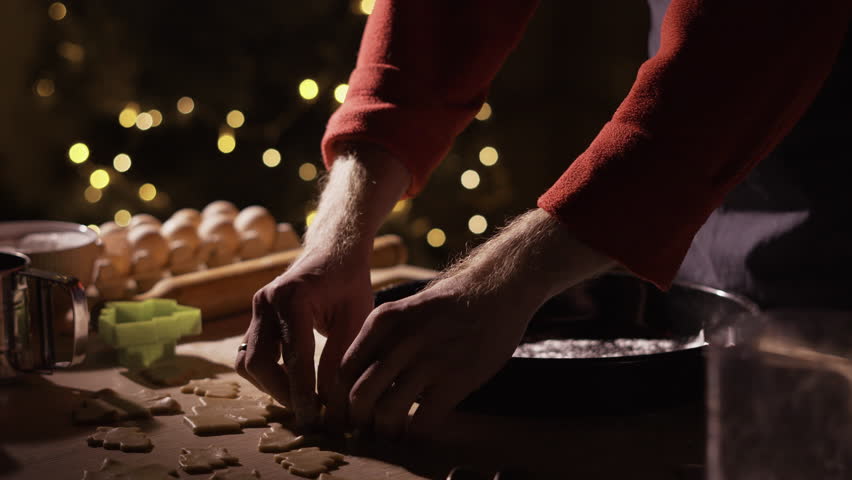 Man making gingerbread cookies in kitchen decorated for Christmas, placing cut out cookies in shape of Christmas tree