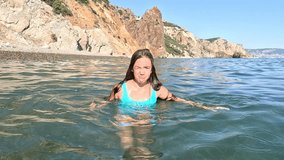 A woman in a blue swimsuit floats in clear water, eyes closed, arms outstretched. A rocky coastline is in the background. Summer holiday vacation and travel concept - Powered by Shutterstock - Get 15% off with code: PIKWIZARD15