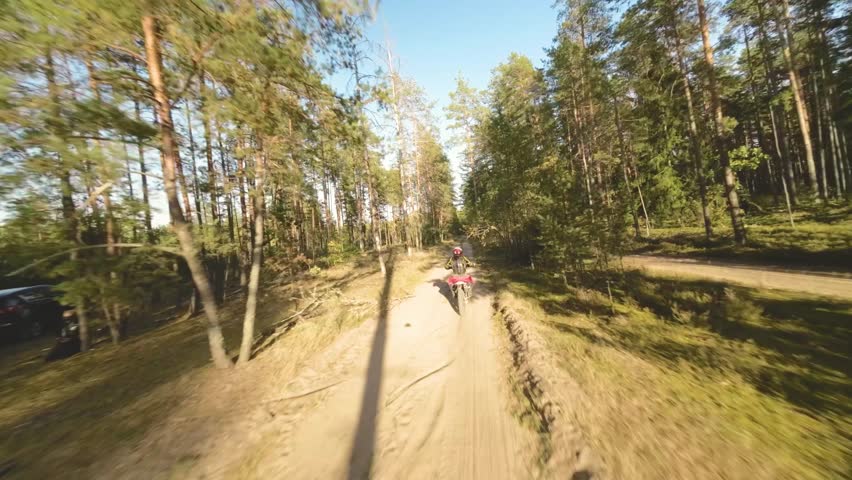 Aerial FPV footage of professional motorcyclist wearing equipment riding light enduro bike trough the sunny summer forest. Motocross sport, off-road motorcycle race adventure.