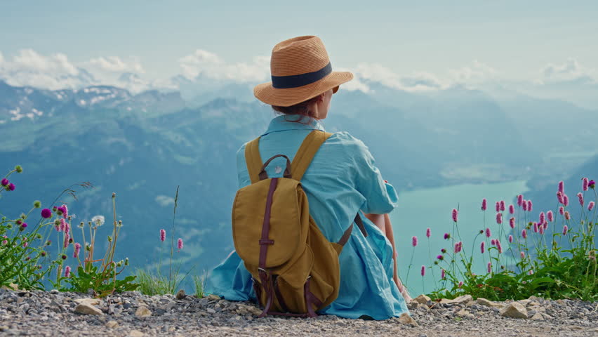 Woman sitting on top a mountain in the Alps, inhales fresh air enjoys an epic view of the mountains. Switzerland