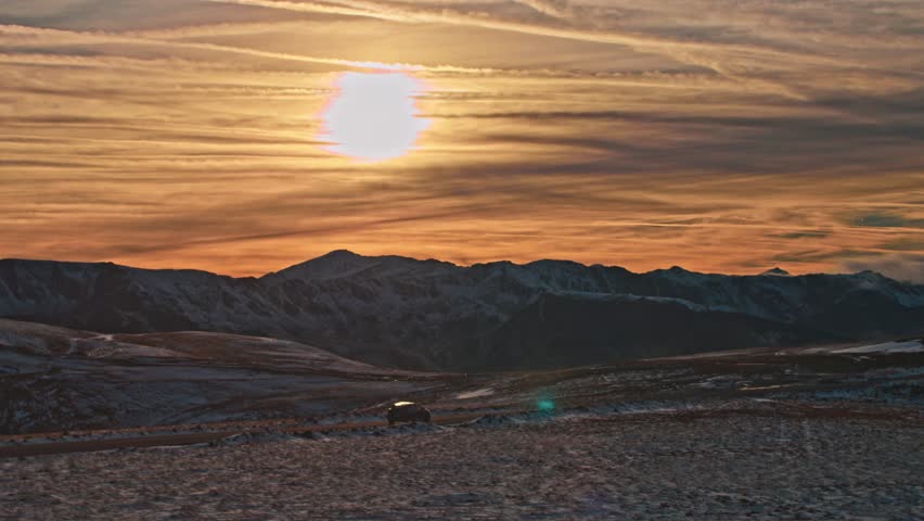 Establishing aerial rolling shot of electric car driving on mountain road. Car driving on empty road with snow white mountains and beautiful sunset view