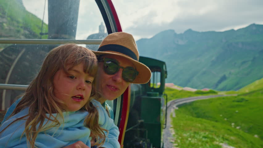 A mother and her little daughter ride in the famous red rotary steam train leaving the town of Brienz in the Swiss Alps along the alpine meadows to the top of a mountain in summer. Switzerland
