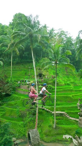 Two riders are cycling on a cable wire above lush green rice terraces in Ubud, showcasing adventure amidst nature.