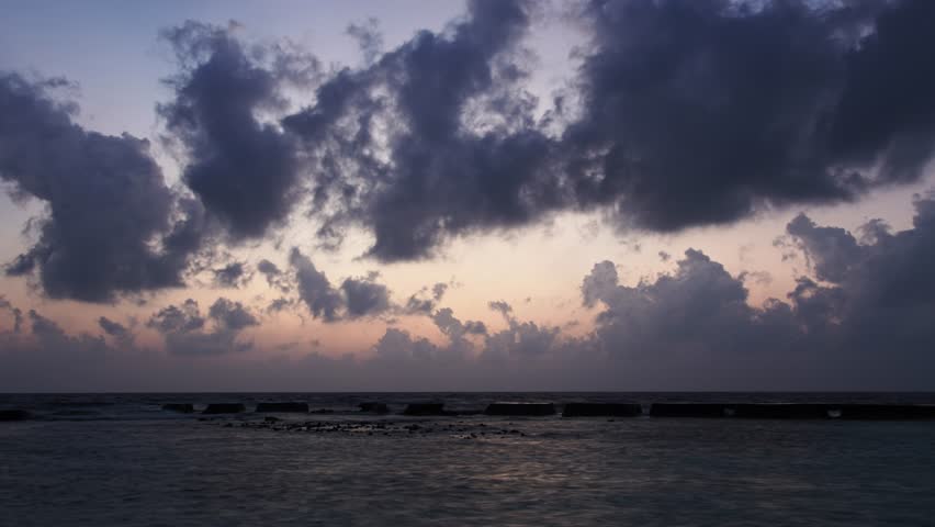 A time-lapse footage of the clouds moving in the dusk sky over the breakwater at the shore of Ellaidhoo Island at sunset, The Maldives