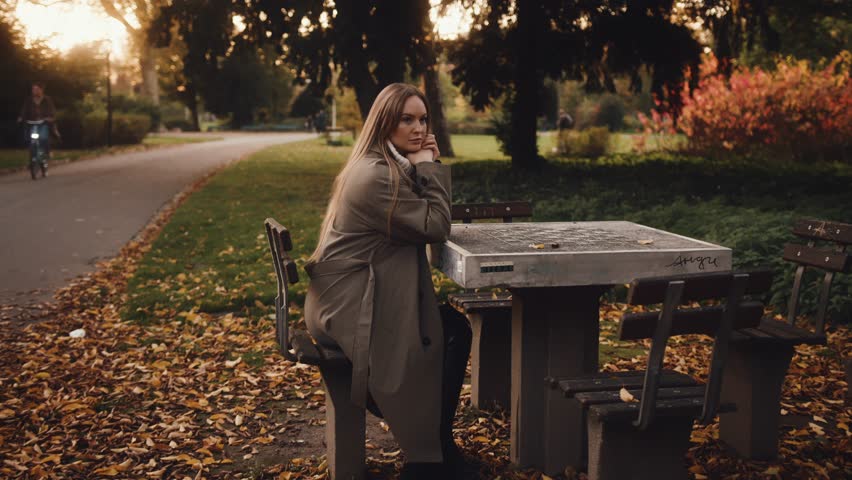 young Ukrainian woman of European appearance with long natural blond hair walks in autumn park in stylish fashionable clothes trench coat skirt boots. quality shooting at sunset. women fashion Germany