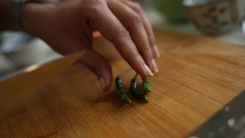 Chef cutting raw chilies in groups on chopping board.