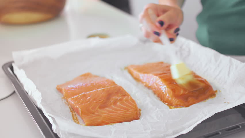 Fresh salmon fillets are being prepared on a baking tray lined with parchment paper. Person is seen adding seasoning, highlighting a simple yet tasty culinary process.