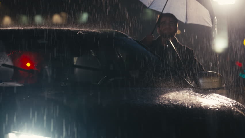 Handsome young man closes his umbrella and enters a car amidst a heavy rainstorm, with raindrops cascading down. Concept of shelter, transition, and resilience against harsh weather.