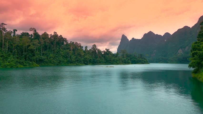 Cheow Lan Lake at sunrise showcases stunning rock formations surrounded by lush greenery and tranquil waters under dramatic skies.