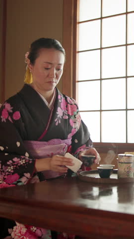 Mature woman, tea and kimono in Japan for serving, traditional drink and cultural hospitality in home. Japanese person, cup and matcha in living room for offer, detox beverage or preparation at table