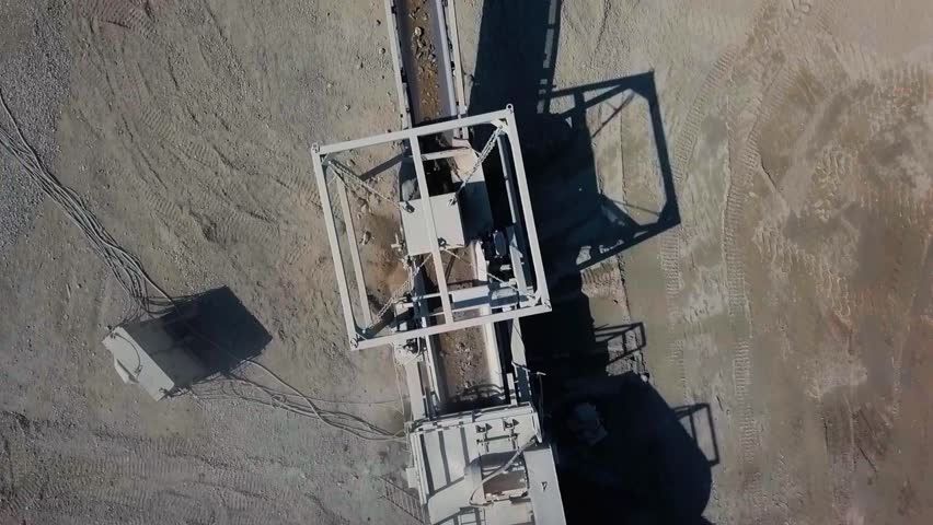 Rocks travel up and tumble down different conveyor belts in a quarry on a sunny day