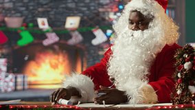 Black Santa opening and reading letters sitting cozy in his log cabin. Winter holiday season brings the magic of wish lists, presents and tradition, spreading Christmas spirit. Camera B. - Powered by Shutterstock - Get 15% off with code: PIKWIZARD15