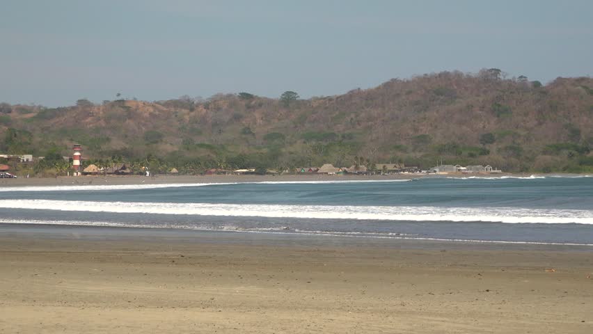 Waves crash on a tropical beach cove with a small town and a lighthouse