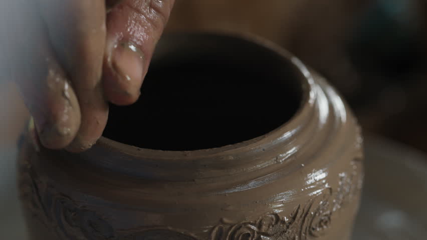 Close up hand of unrecognizable person guiding another human's finger to forming even edges of patterned jug before baking. Creator giving master class of making high quality products at studio.