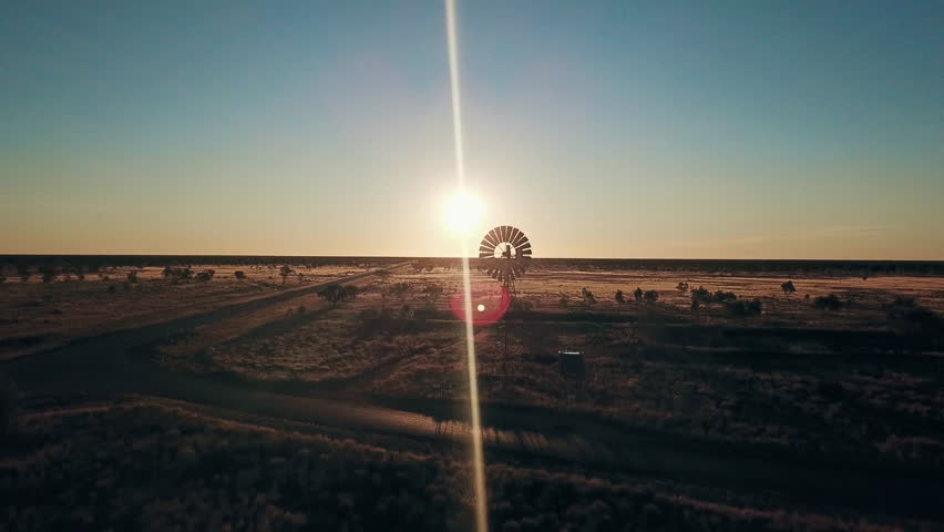 Aerial view. Silhouette of a large windmill in central Australia rotating in slow motion against dramatic Australian outback sunset. No people. Red center Uluru