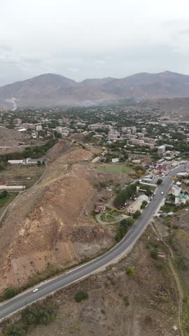 Vertical drone shot along a scenic road between rocky hills and green trees