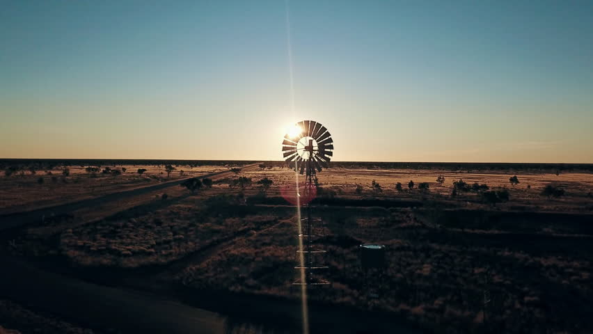 Aerial view. Silhouette of a large windmill in central Australia rotating in slow motion against dramatic Australian outback sunset. No people. Red center Uluru