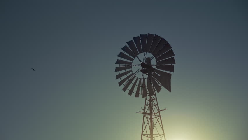 Silhouette of a large windmill in central Australia rotating in slow motion against dramatic Australian outback sunset. No people. Red center Uluru