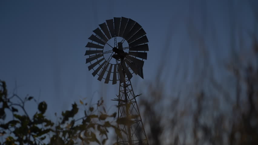 Silhouette of a large windmill in central Australia rotating in slow motion against dramatic Australian outback sunset. No people. Red center Uluru