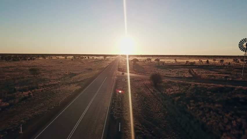 Aerial view. Silhouette of a large windmill in central Australia rotating in slow motion against dramatic Australian outback sunset. No people. Red center Uluru