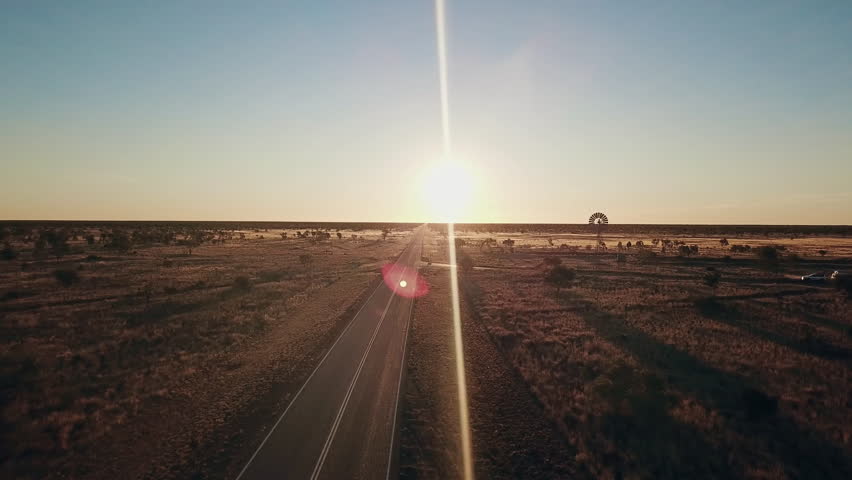 Aerial view. Silhouette of a large windmill in central Australia rotating in slow motion against dramatic Australian outback sunset. No people. Red center Uluru