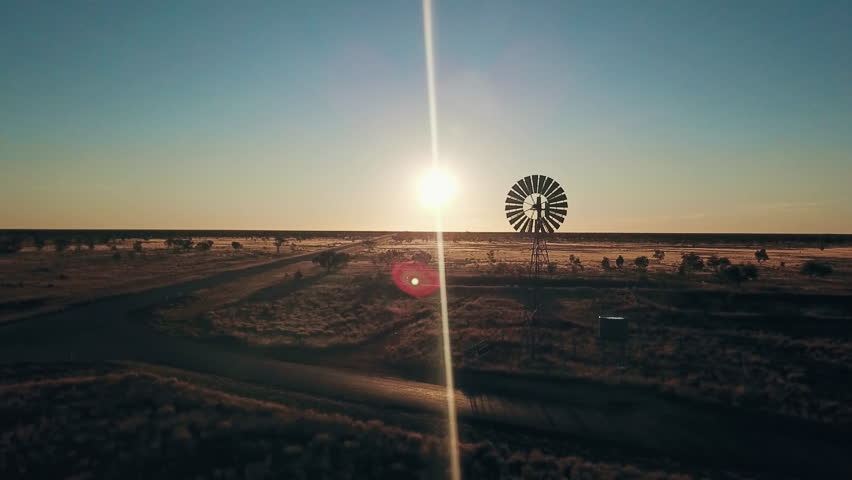 Aerial view. Silhouette of a large windmill in central Australia rotating in slow motion against dramatic Australian outback sunset. No people. Red center Uluru
