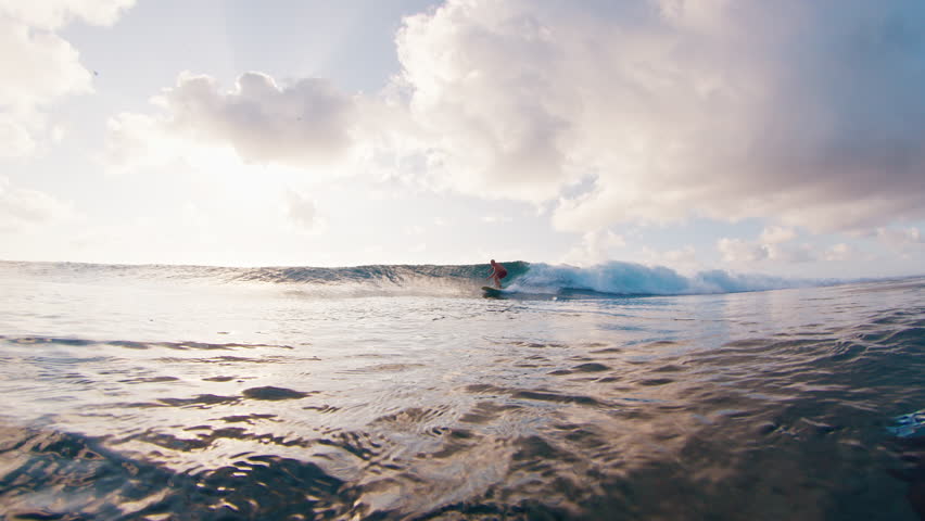 Man surfs the wave and passes by the camera spraying water into the frame