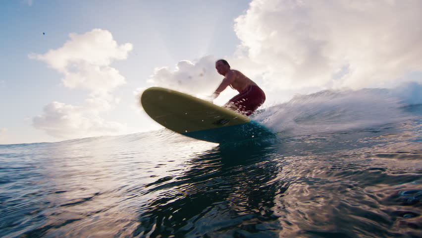 Man surfs the wave and passes by the camera spraying water into the frame