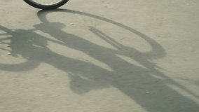 Cyclist wearing sneakers and black trousers pedaling bicycle slowly on a sunny day, creating distinct and clear shadow of the bicycle cast onto the sunlit road - Powered by Shutterstock - Get 15% off with code: PIKWIZARD15