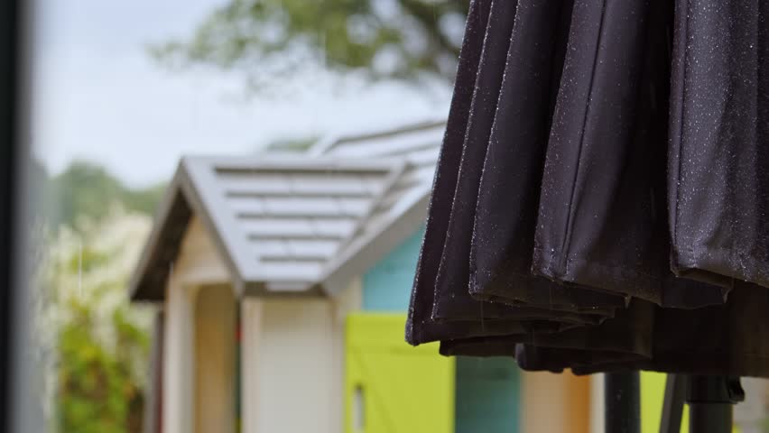 Rainfall over rural homestead with outdoors umbrella, static view