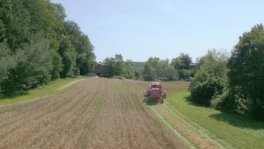 An aerial footage over a Combine farmer harvesting Wheat Forest Fields with forest trees in Switzerland