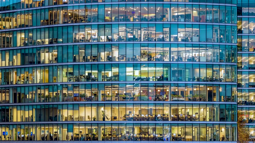 Timelapse panning view of an illuminated office building during evening with workers movement