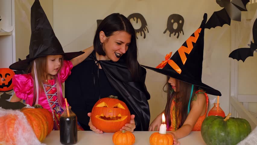 A mother in the guise of a devil and daughters dressed as witches in a room decorated with Halloween decorations