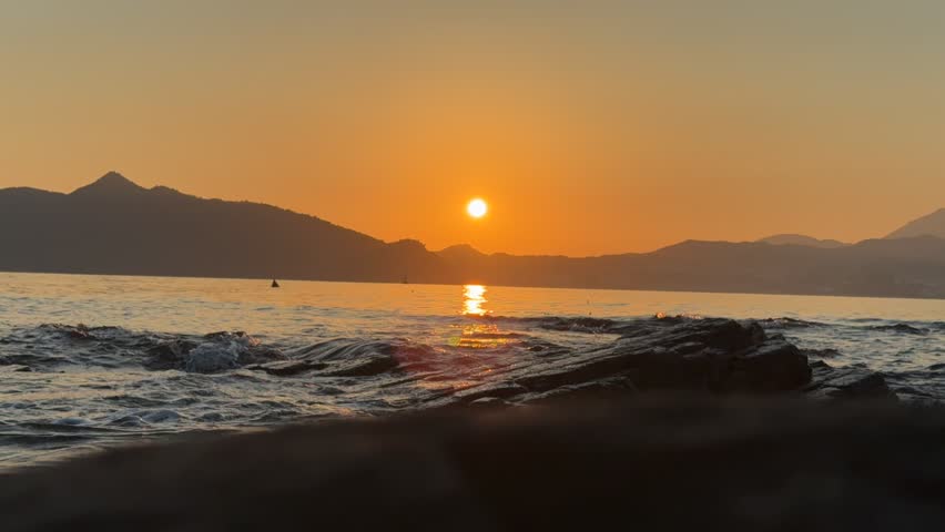 A timelapse of sunrise scene on a rocky shore with silhouetted mountain in the background, a boat crossed the view
