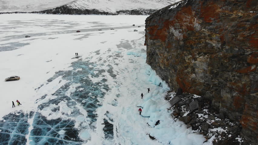 Tourists admire icicles on the huge rocks of Olkhon Island, cars drive on the ice of frozen Lake Baikal. Winter trip.  