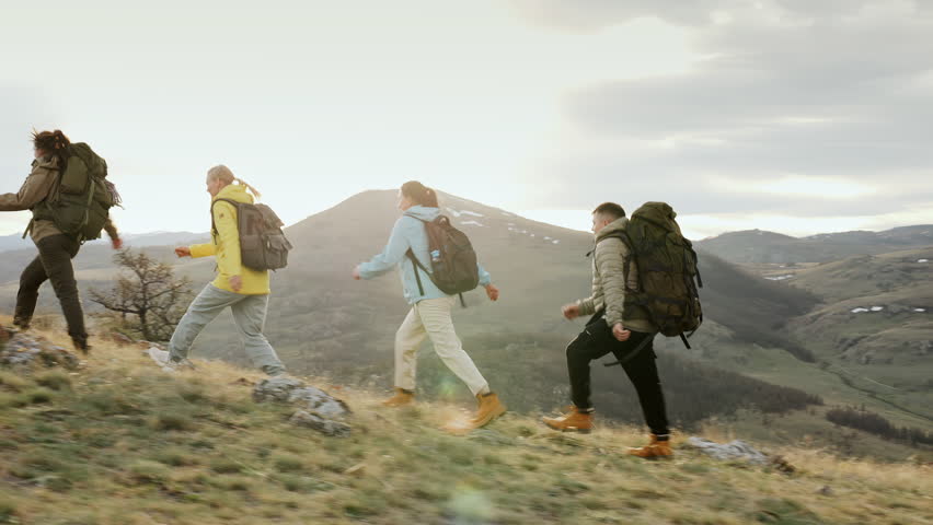Group of four hikers with backpack together go trail forward high up at scenic mountain landscape views. Active uphill path, climbing way and travel recreation