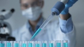 Female scientist researcher wearing a lab coat, mask, and safety glasses is using a micropipette to drop a blue liquid into a test tube, close up view. Medicine and science concept - Powered by Shutterstock - Get 15% off with code: PIKWIZARD15
