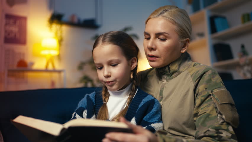 Service member mother and her little daughter reading together, upbringing